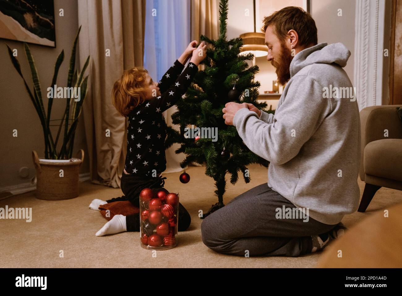 Zenzero padre e figlio in abbigliamento casual decorazione albero di Natale in accogliente soggiorno Foto Stock