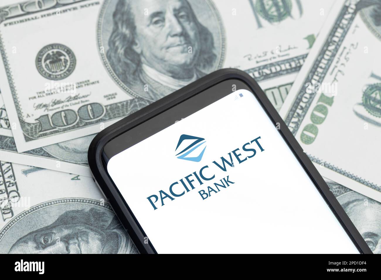 Galizia, Spagna; 12 marzo 2023: Logo della società Pacific West Bank Financial Services sullo schermo dello smartphone e sfondo delle banconote in dollari Foto Stock