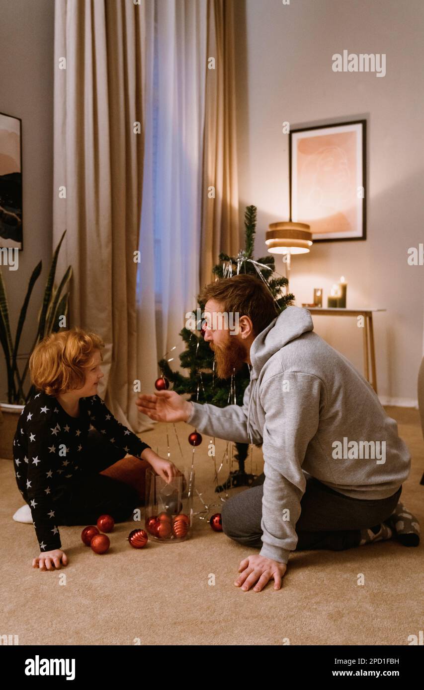 Il padre ed il figlio piccolo carino che decorano l'albero di Natale in salotto accogliente a casa Foto Stock