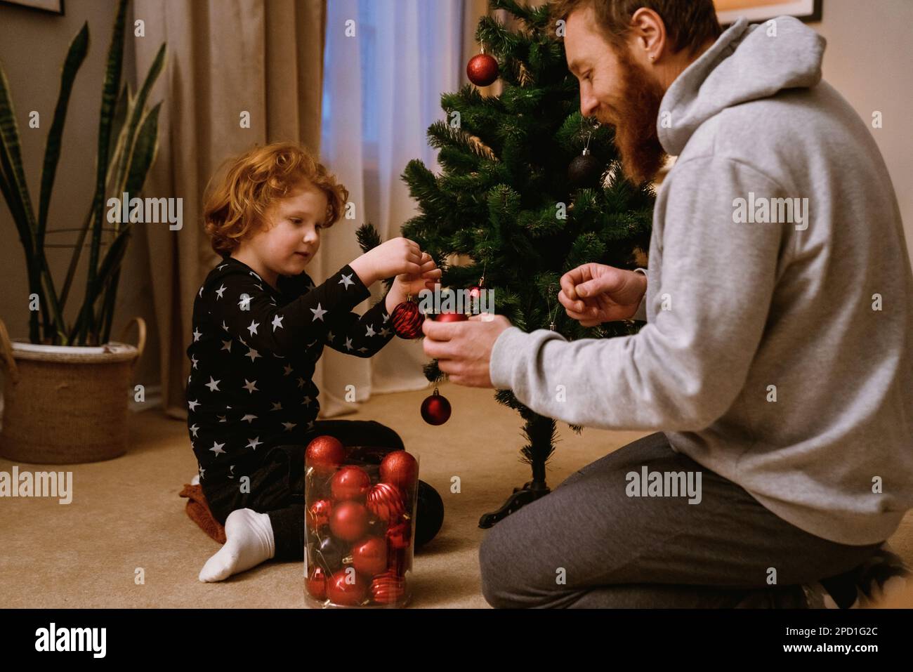 Il padre ed il figlio piccolo carino che decorano l'albero di Natale in salotto accogliente a casa Foto Stock