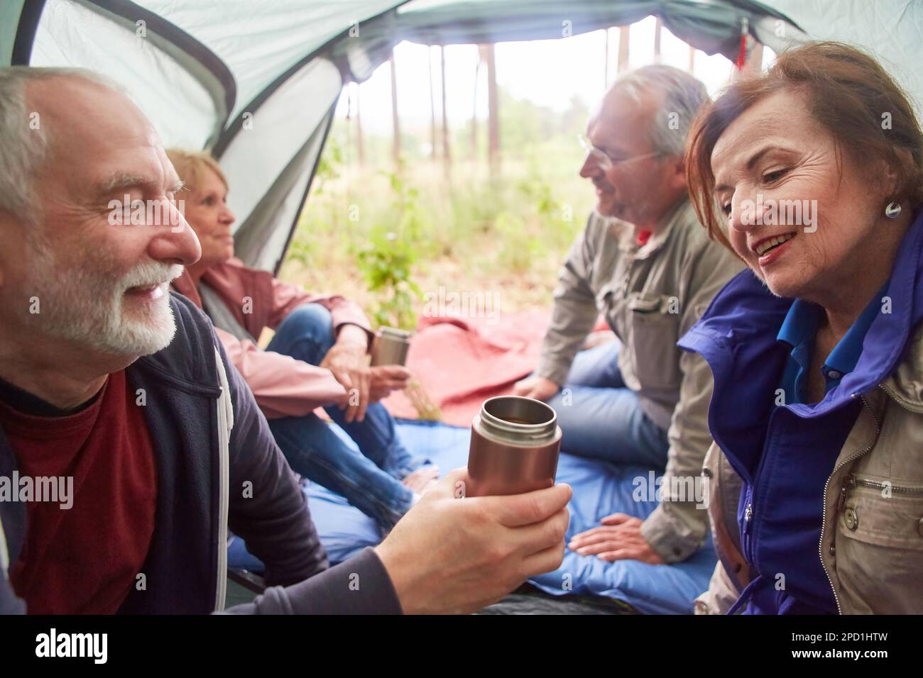 Le coppie anziane sorridenti parlano mentre trascorrono il tempo libero in una tenda da campeggio durante le vacanze Foto Stock