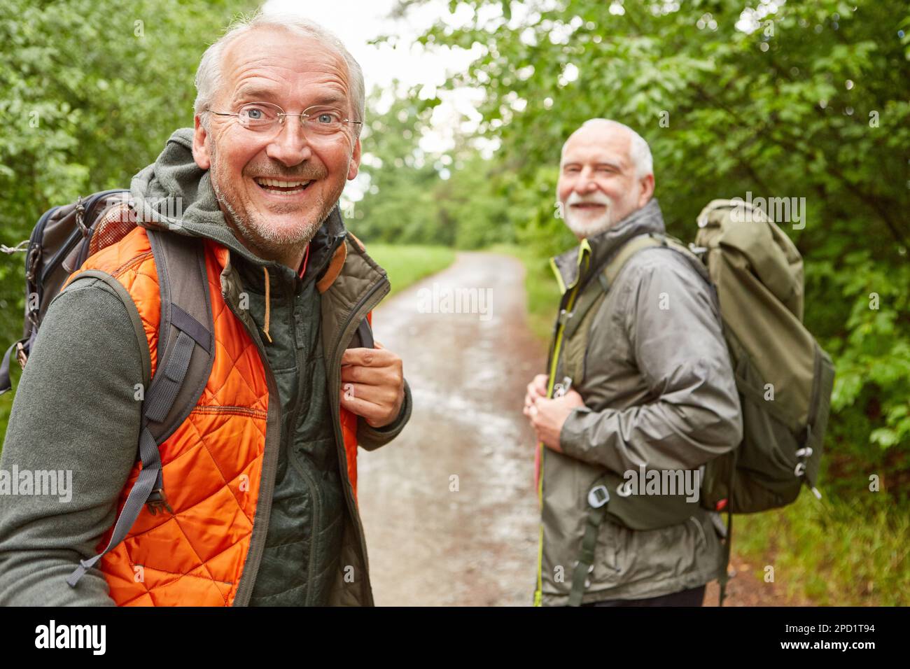 Ritratto di felice uomo anziano con amico maschio in background escursioni a piedi nella foresta durante la ragione piovosa Foto Stock