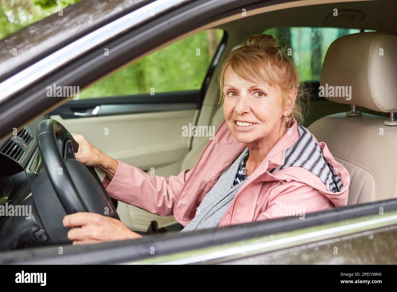 Donna anziana sorridente che guida l'auto in natura Foto Stock