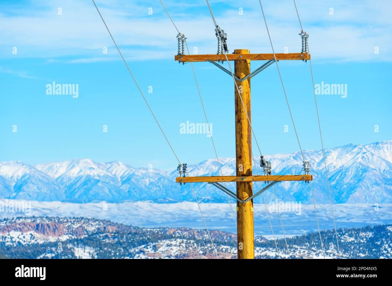 Palo di potenza in legno con fili sullo sfondo di cime innevate e un cielo blu chiaro. Energia, alimentazione, tecnologia e motore Foto Stock
