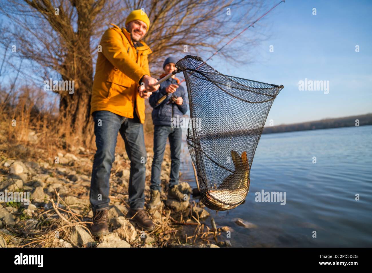 Padre e figlio pescano nella soleggiata giornata invernale. Hanno pescato un pesce e lo tengono in una rete di sbarco. Foto Stock