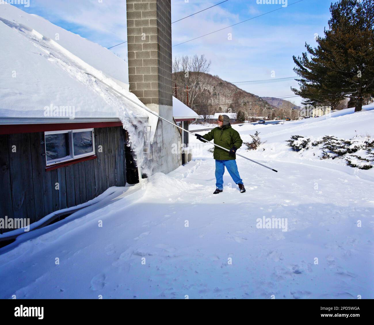 Un uomo usa un rastrello per sgombrare un tetto coperto di neve in Vermont, USA Foto Stock