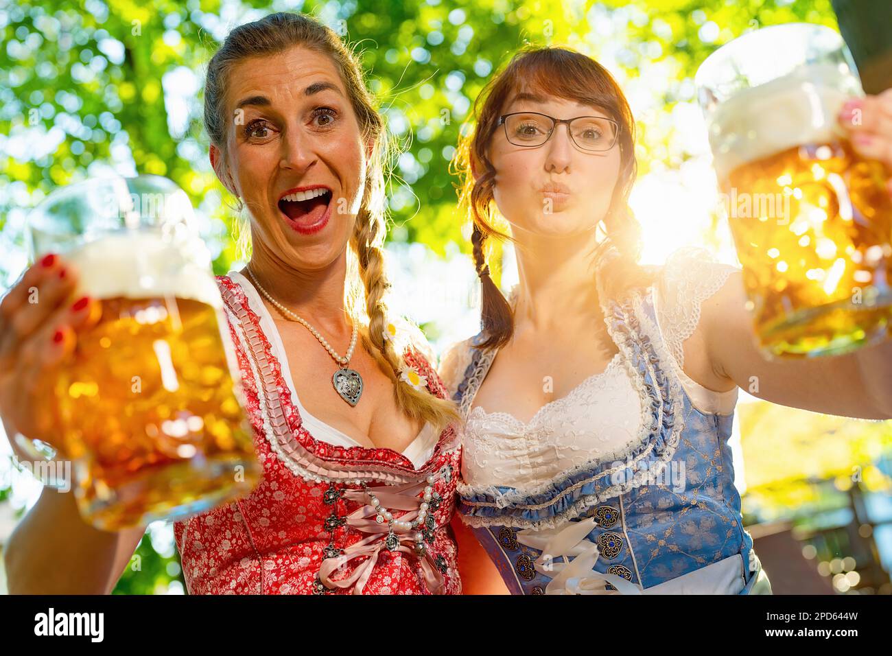 I girlfriends che osservano e urlano, baciano alla macchina fotografica dicono i saluti o gli occhiali di clinking con la tazza della birra nella birreria bavarese della birra o nell'oktoberfest Foto Stock