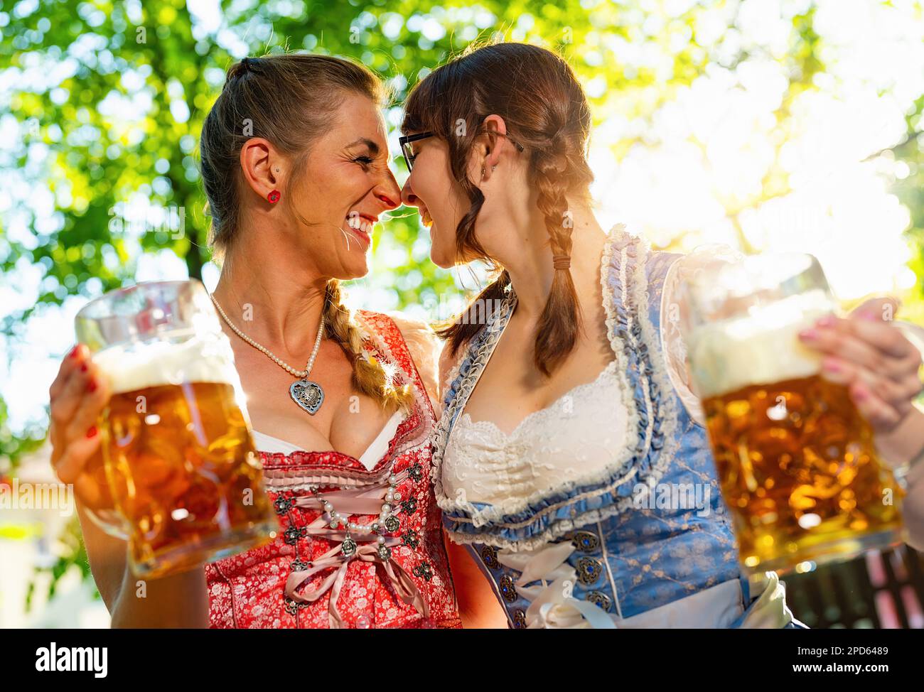 I girlfriends che si sfregano il naso alla macchina fotografica dicono i saluti o i bicchieri da clinking con la tazza di birra nella birreria all'aperto bavarese o nell'oktoberfest Foto Stock