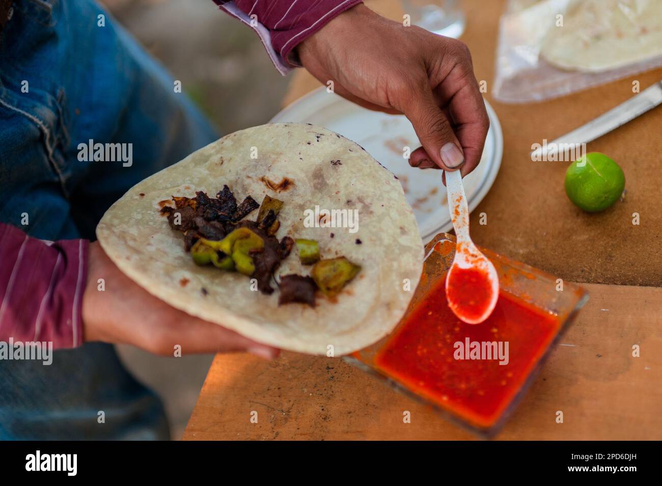 Un rancher messicano versa la salsa al peperoncino piccante, a base di peperoncino, sulla carne alla griglia nella tortilla durante una pausa pranzo in una fattoria vicino a Baviácora, Messico. Foto Stock