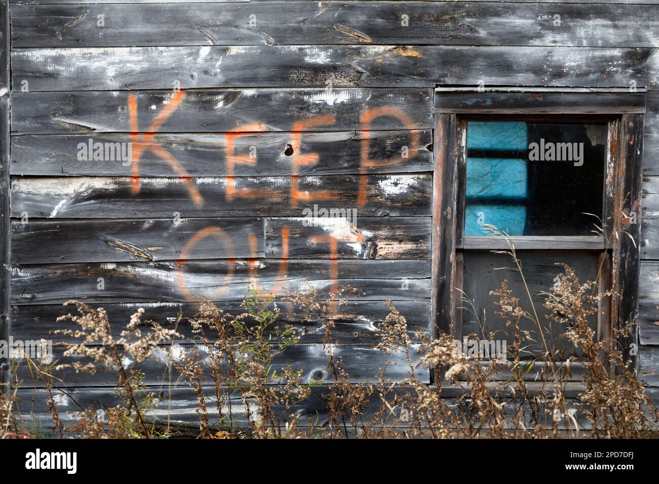 Uno spray di avvertenza da tenere fuori dipinto sul lato di un vecchio edificio in legno intatto. Foto Stock
