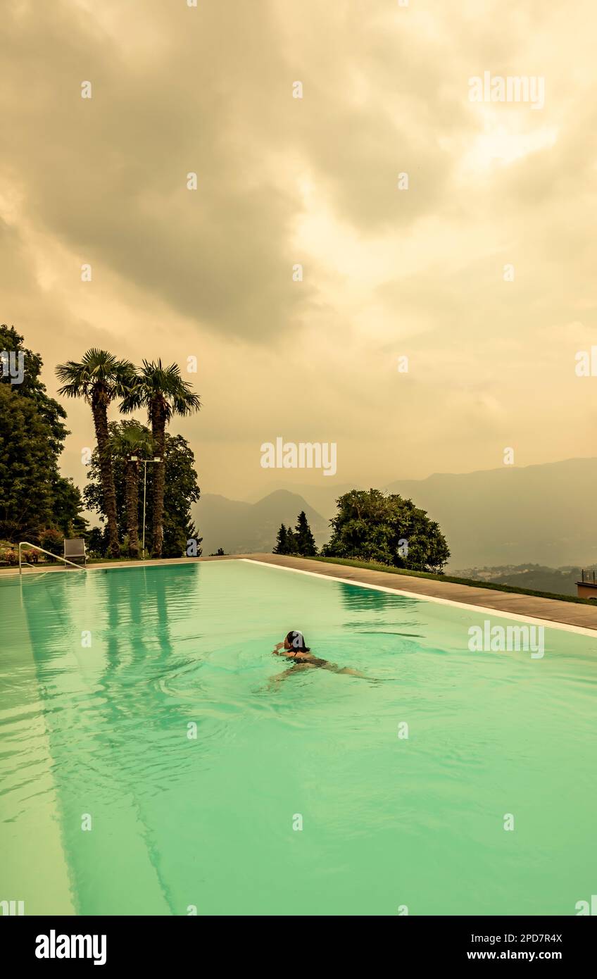 Donna nuotare in piscina con vista panoramica con montagna in Ticino, Svizzera. Foto Stock Donna nuotare in piscina con vista panoramica con montagna in Ticino, Svizzera. Foto Stock