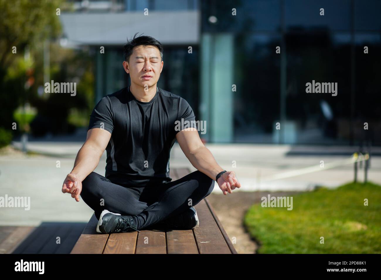 L'uomo asiatico medita nella posizione del loto, l'uomo nel parco vicino al lago esegue esercizi di yoga, lo sportivo si riposa con un mento chiuso dopo esercizi fisici attivi e corsa. Foto Stock