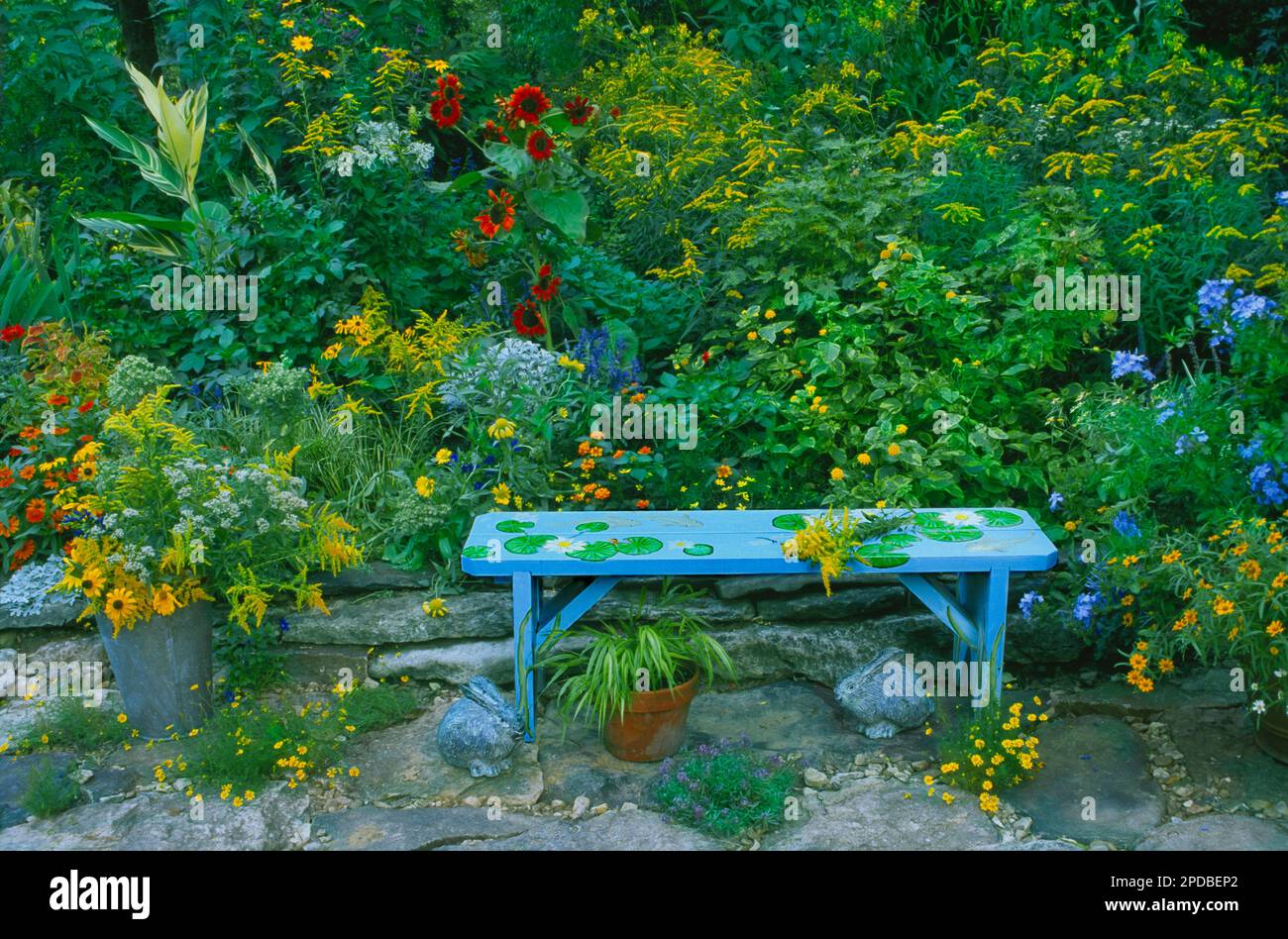 Una panchina blu decorata e dipinta fantasiosamente con immagini del giardino seduto su un patio di roccia in un giardino fiorito in estate, Missouri, Stati Uniti Foto Stock