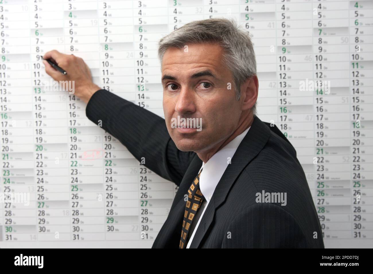 uomo d'affari che inserisce appuntamenti in un calendario da parete Foto Stock