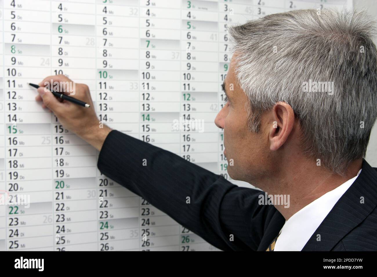 uomo d'affari che inserisce appuntamenti in un calendario da parete Foto Stock