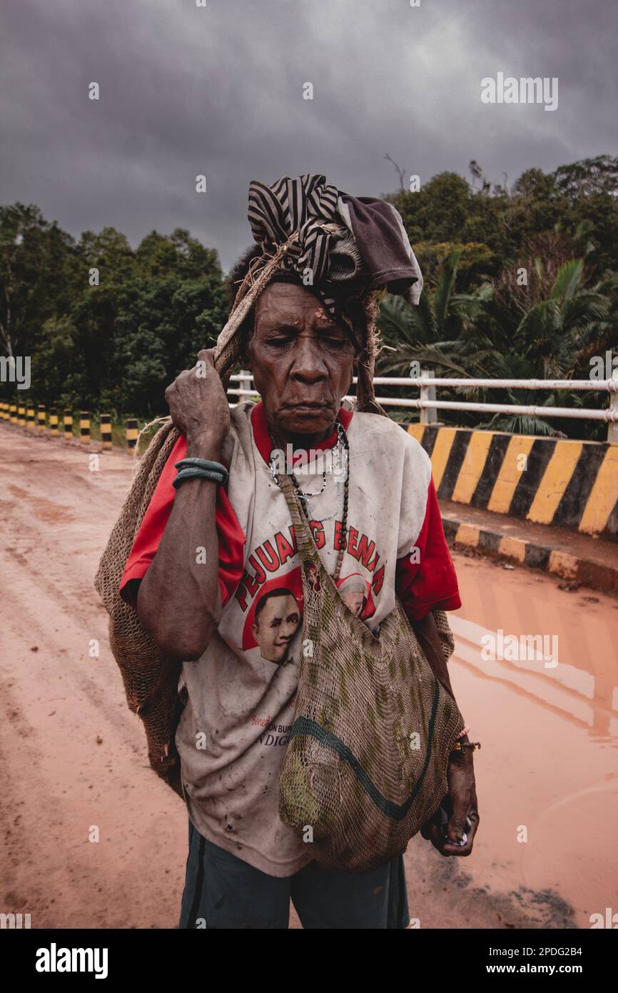 Una donna anziana che porta una borsa cammina nell'interno di Papua durante i cieli nuvolosi, Indonesia, il 2017 settembre Foto Stock