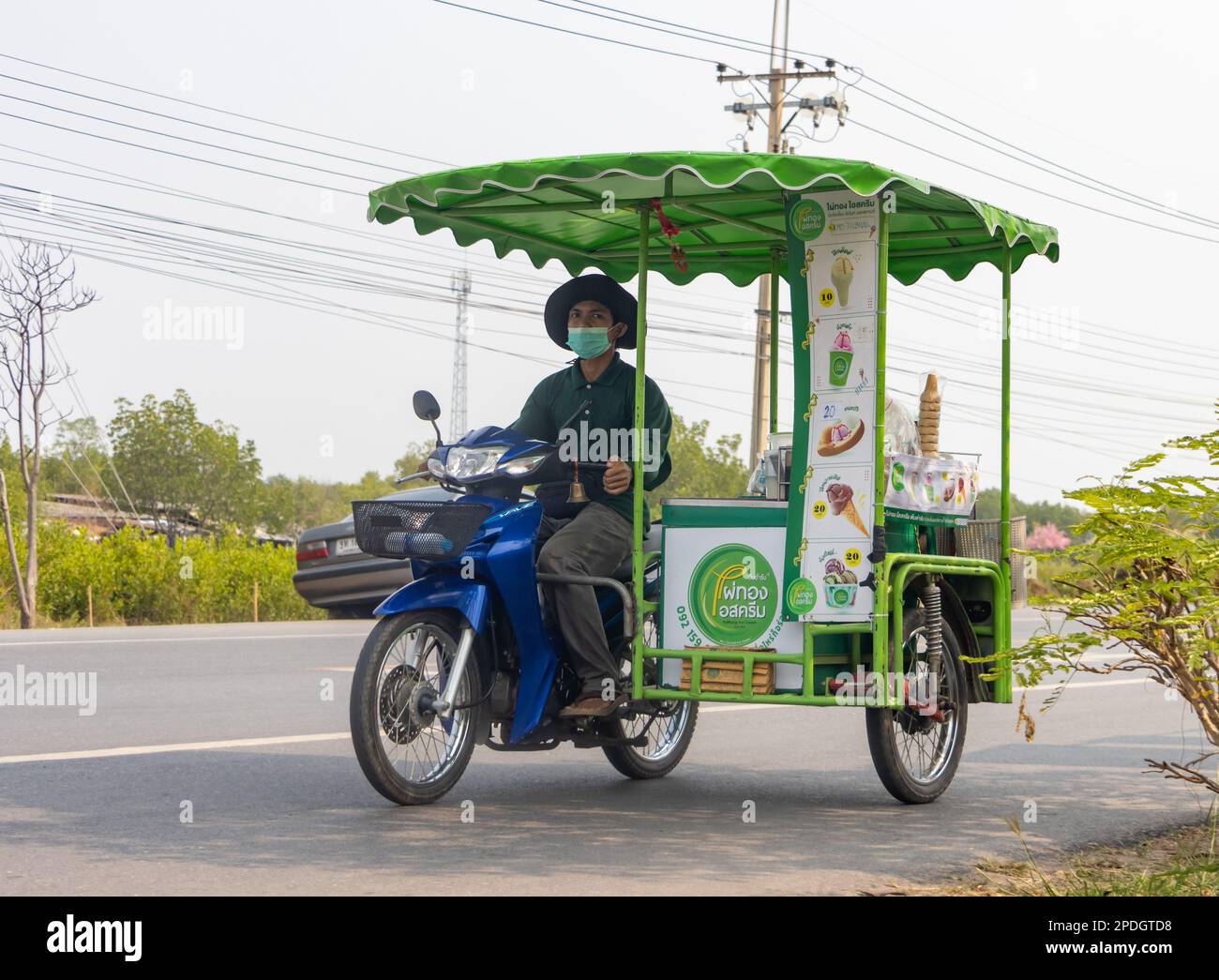 BANGKOK, THAILANDIA, MAR 11 2023, un fornitore di gelati guida una moto a tre ruote lungo una strada del villaggio Foto Stock