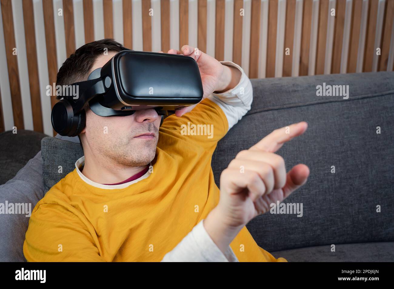 Sorridente adulto maschio indossando occhiali VR preme con il dito sull'interfaccia per la realtà virtuale a casa, gioco, tecnologia, metaverse, visualizzazione 360 vide Foto Stock