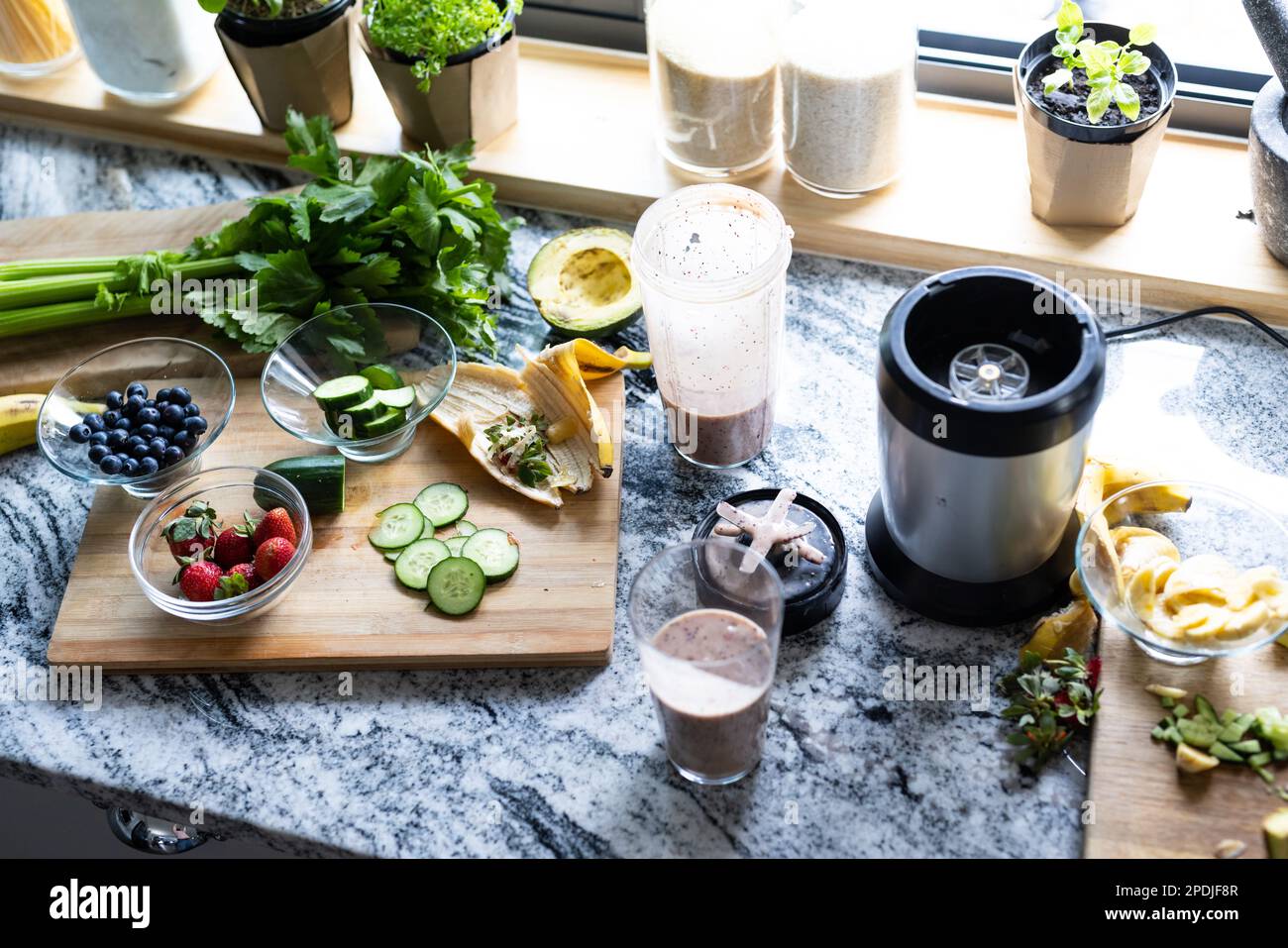 Vista ad angolo alto del frullato in bicchiere e frullatore con frutta ed erbe sul bancone della cucina Foto Stock