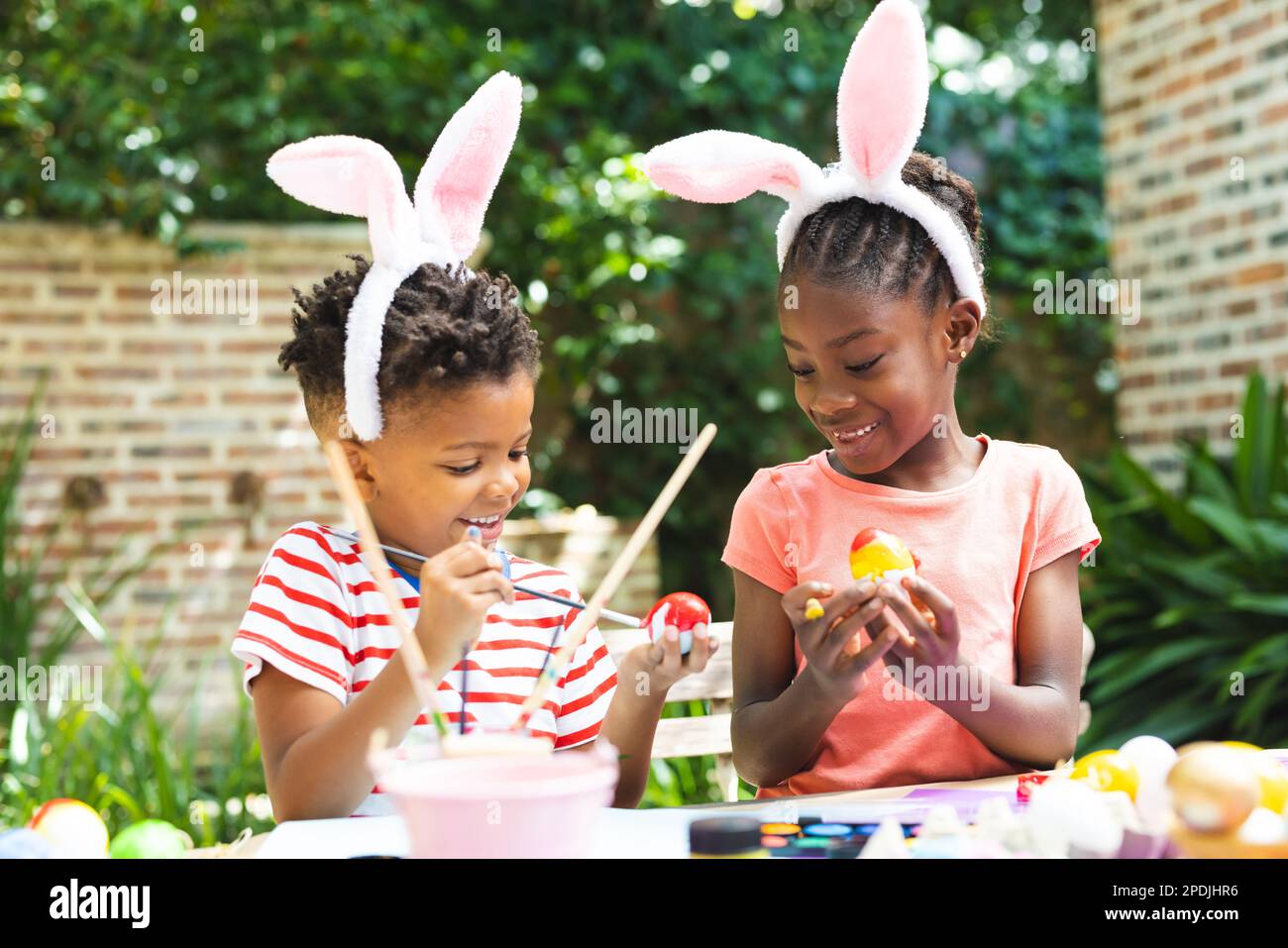 Felici bambini afroamericani colorano le uova di pasqua in giardino Foto Stock
