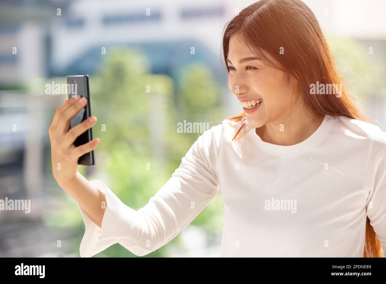 le persone amano usare le videochiamate via internet buon sorriso. Donna asiatica che guarda lo smartphone sorridendo all'aperto. Foto Stock