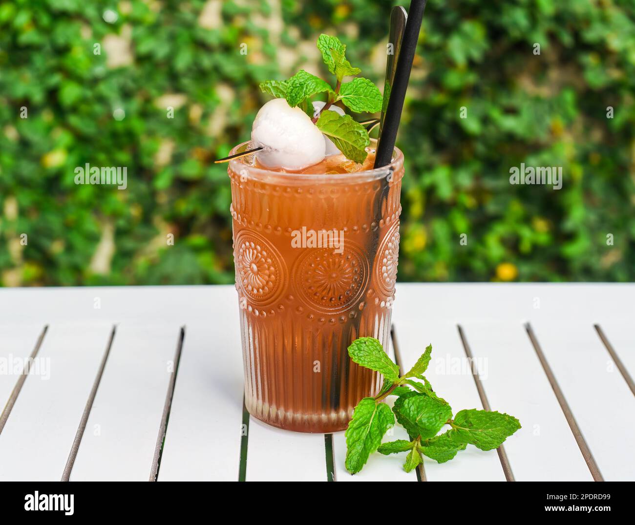 Tè verde ghiaccio con lychee e menta su tavolo di legno bianco contro foglie verdi con spazio copia Foto Stock