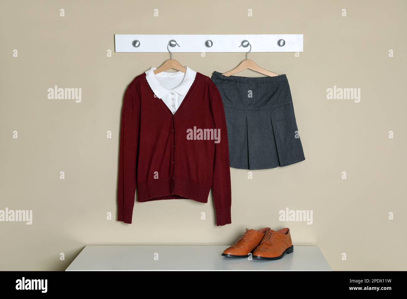 Camicia, jumper e gonna appesi alla parete beige. Uniforme scolastica Foto Stock