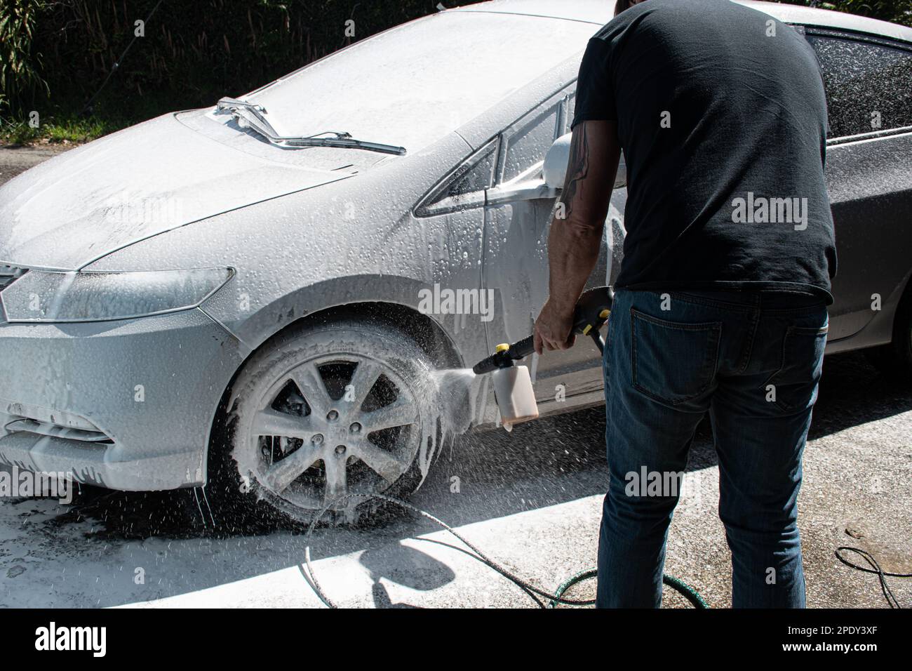 due morbillo per la pulizia di un'auto argentata spruzzando una schiuma con una idropulitrice per il lavaggio di un'auto Foto Stock