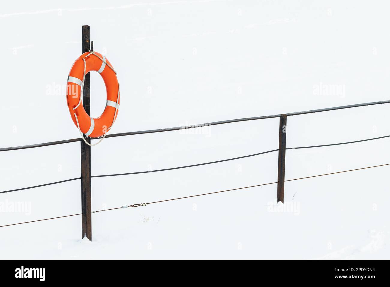 La scialuppa di salvataggio rossa si trova su una ringhiera sulla costa ghiacciata del lago in una giornata invernale Foto Stock