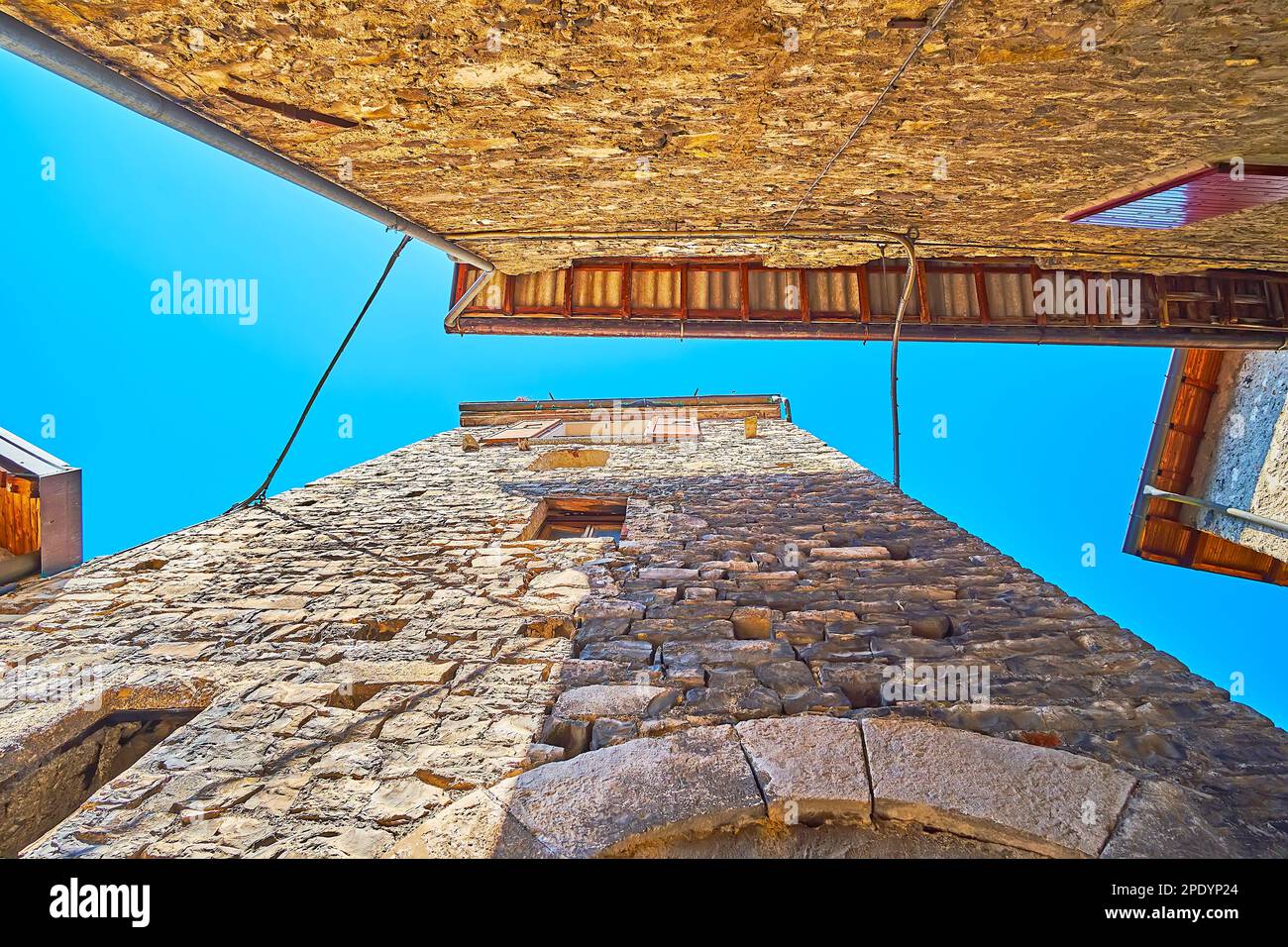 Le alte case in pietra sulla stretta strada con un cielo azzurro, visto attraverso il divario tra loro, Albogasio, Valsolda, Italia Foto Stock