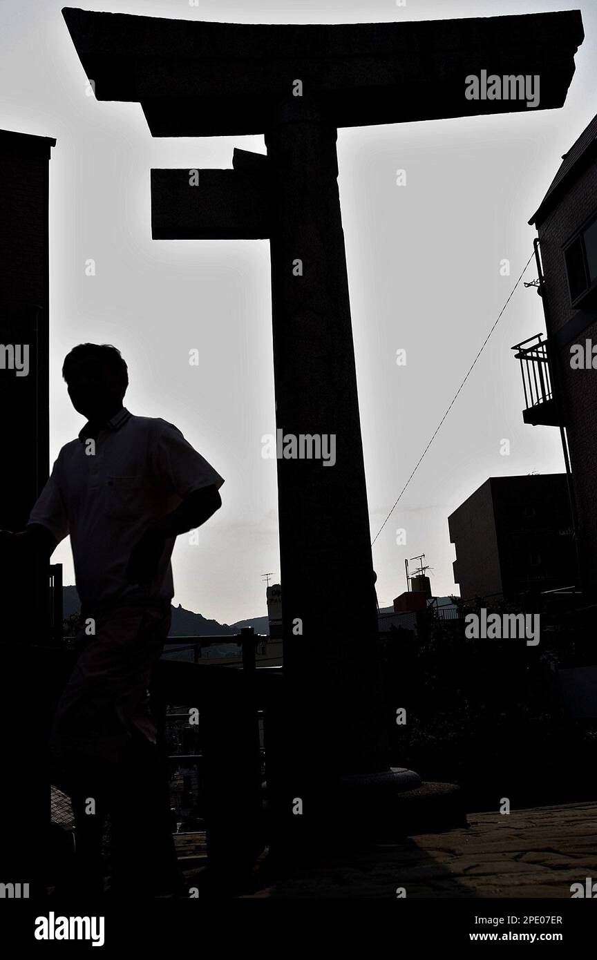 A man walks past a Shinto shrine's old "Torii" gate in the residential quarter in Nagasaki, western Japan, Sunday, July 31, 2005. The gate was preserved the way it was at the time when a plutonium bomb "Fatman" exploded overhead on Aug 9, 1945. The gate was blown off and split in two but the right half of the gate remained intact. Nagasaki marks the 60th anniversary Aug 9. (AP Photo/Junji Kurokawa) Foto Stock