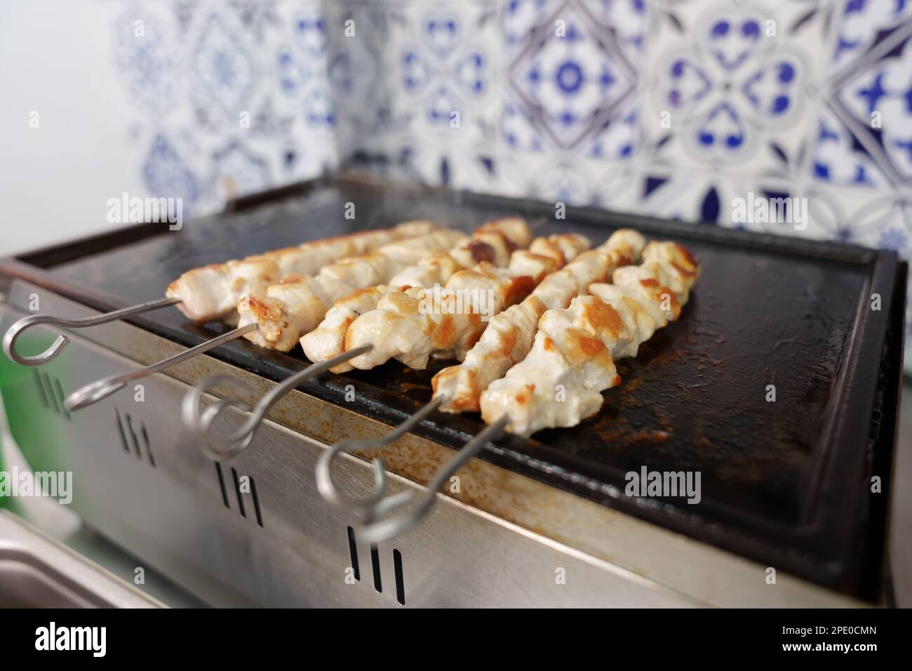 Carne di pollo su spiedini che cucinano su una padella alla griglia calda in un ristorante greco fast food. Foto ravvicinata del filetto di pollame che viene cucinato per pranzo Foto Stock
