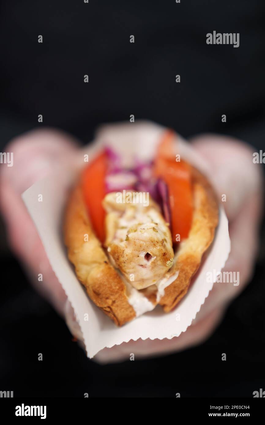 Il cuoco che tiene hot dog esotico preparato con carne di pollo marinata cotta alla griglia e servito con cipolla rossa e salsa calda in cuccette croccanti Foto Stock