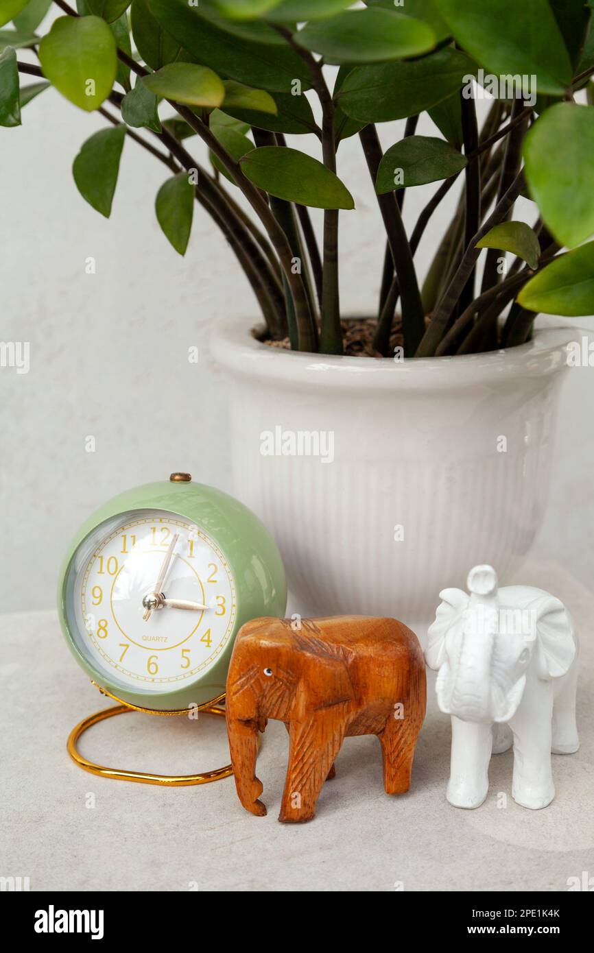 Sveglia verde in stile vintage che mostra l'ora nel pomeriggio. Elegante orologio rotondo, statuette di elefante e una pianta in vaso su un comodino Foto Stock