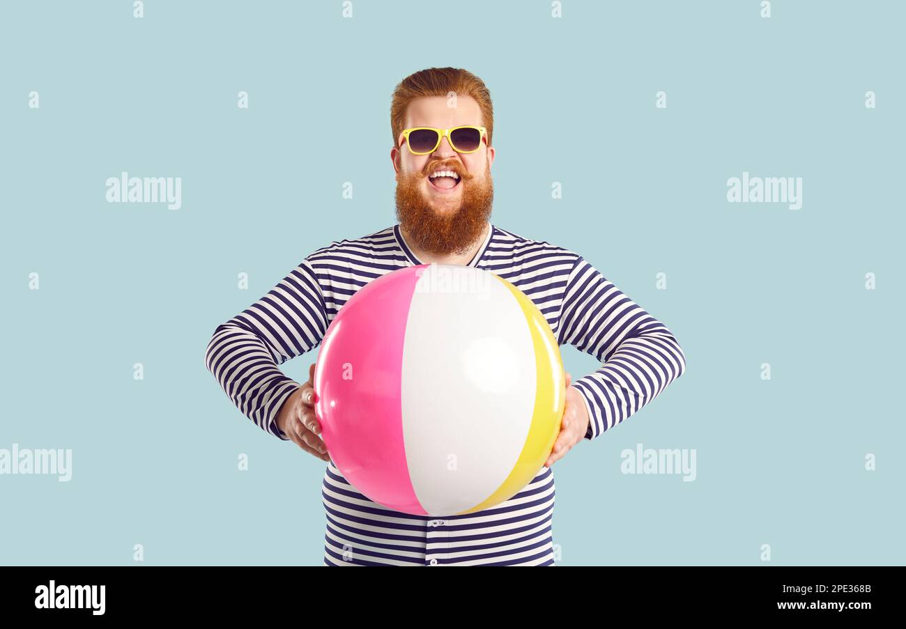 Allegro divertente uomo grasso bearded che si diverte con palla gonfiabile su sfondo blu chiaro pastello. Foto Stock