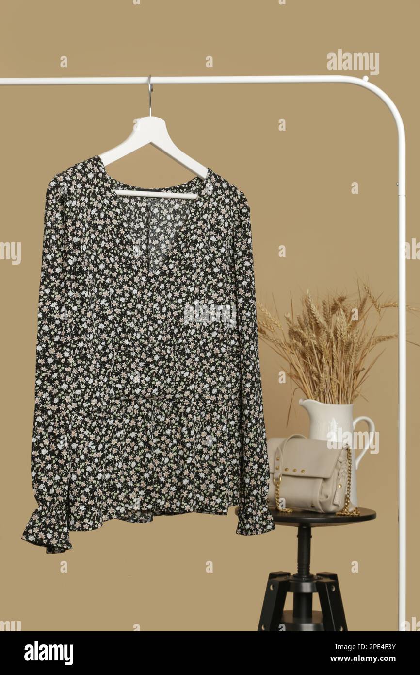 Abiti da donna. Appendiabiti con elegante blusa floreale scura e borsa a tracolla in pelle su appendiabiti. Capo di moda senza tempo di buona qualità. Foto Stock