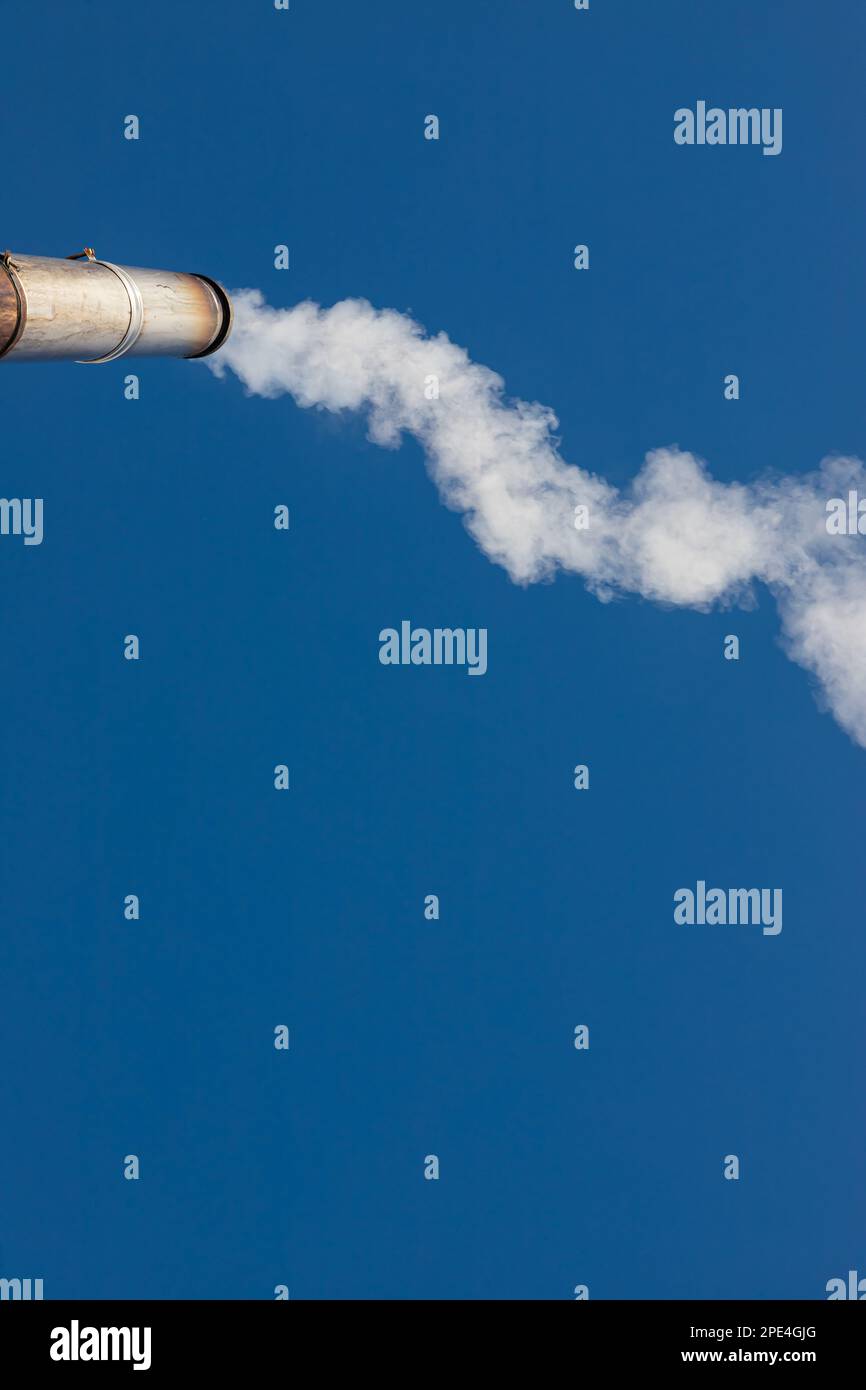 un pennacchio di fumo o di vapore da un'appezzamento industriale su un cielo blu chiaro. Foto Stock