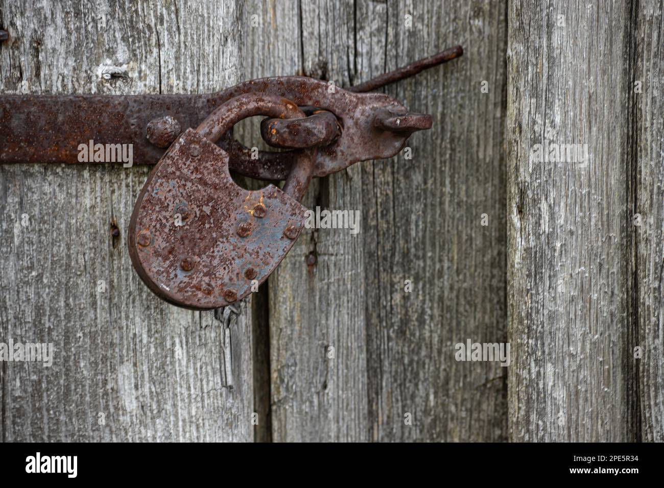Vista ravvicinata del vecchio lucchetto arrugginito su una vecchia porta di legno grigio. Foto Stock