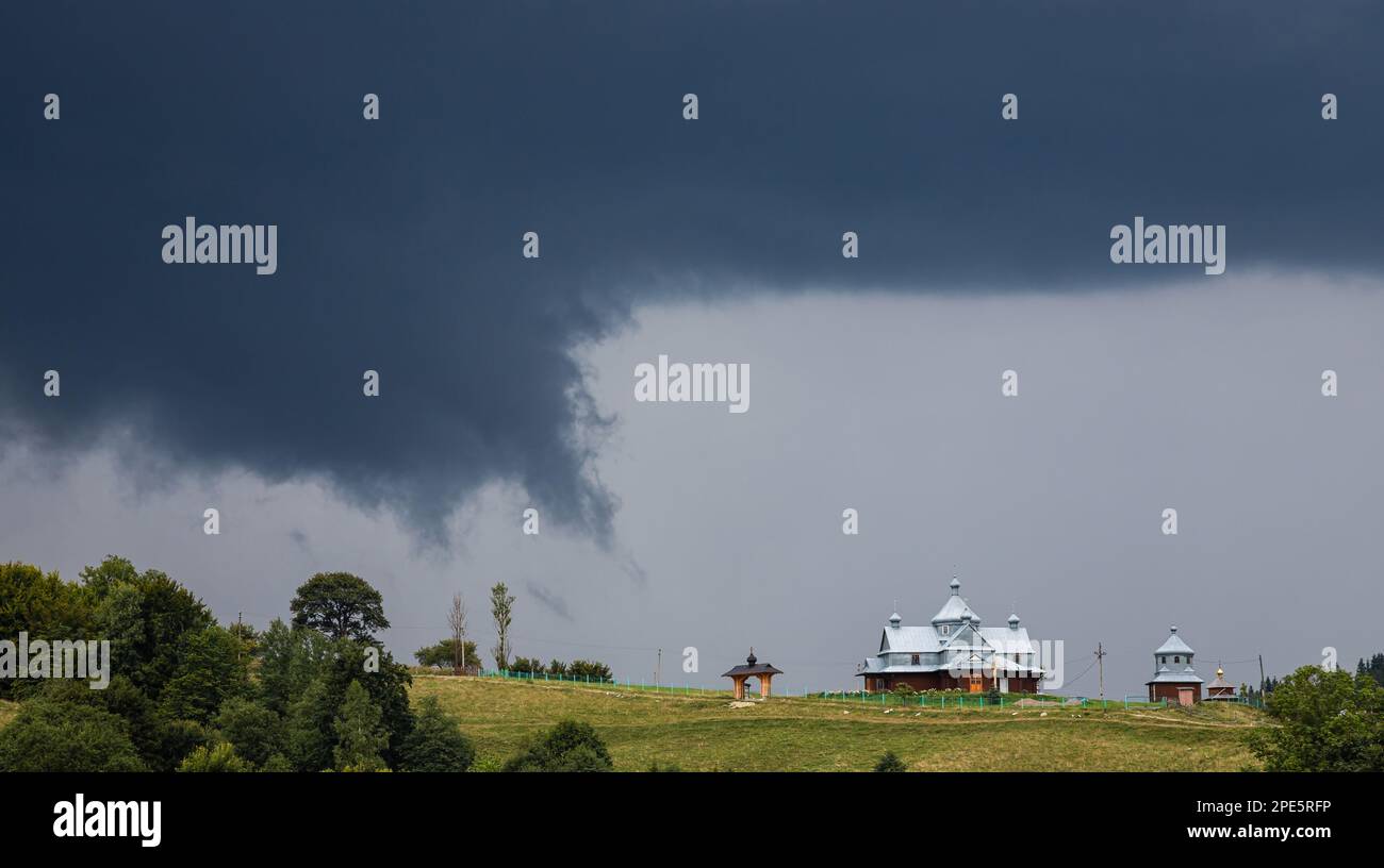 Nuvole tempesta, cielo minaccioso, collina e chiesa, alberi verdi prima della pioggia. Foto Stock