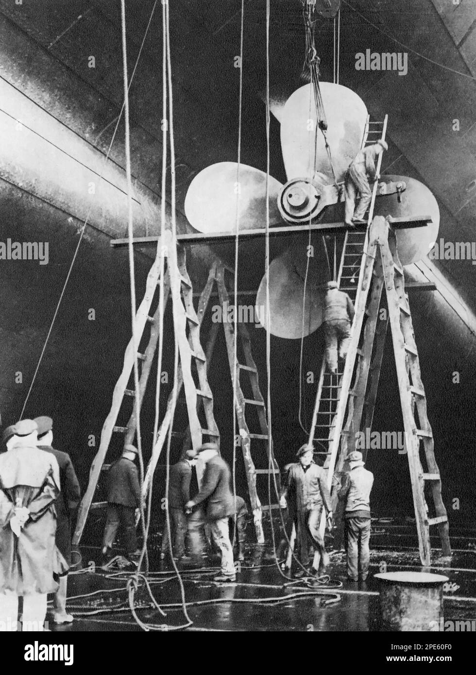 Uomini che lavorano su una delle eliche della White Star Liner RMS Majestic, Southampton, Inghilterra, 1934. Originariamente lanciata nel 1914 come Hamburg America Line SS Bismarck, dopo la prima guerra mondiale, fu terminata dai suoi costruttori tedeschi e consegnata agli alleati come riparazione di guerra e divenne la nave ammiraglia della White Star Line RMS Majestic. Foto Stock