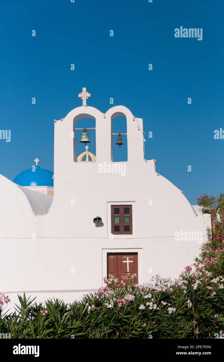 Facciata di una chiesa ortodossa dalle pareti bianche con un fiore di campanile contro il cielo blu sull'isola di Santorini in Grecia Foto Stock