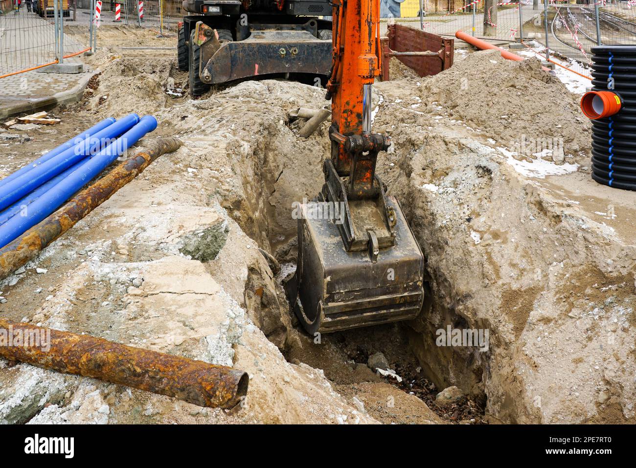 Un escavatore idraulico con benna scava una trincea in una strada cittadina per la sostituzione di tubi di comunicazione sotterranei Foto Stock