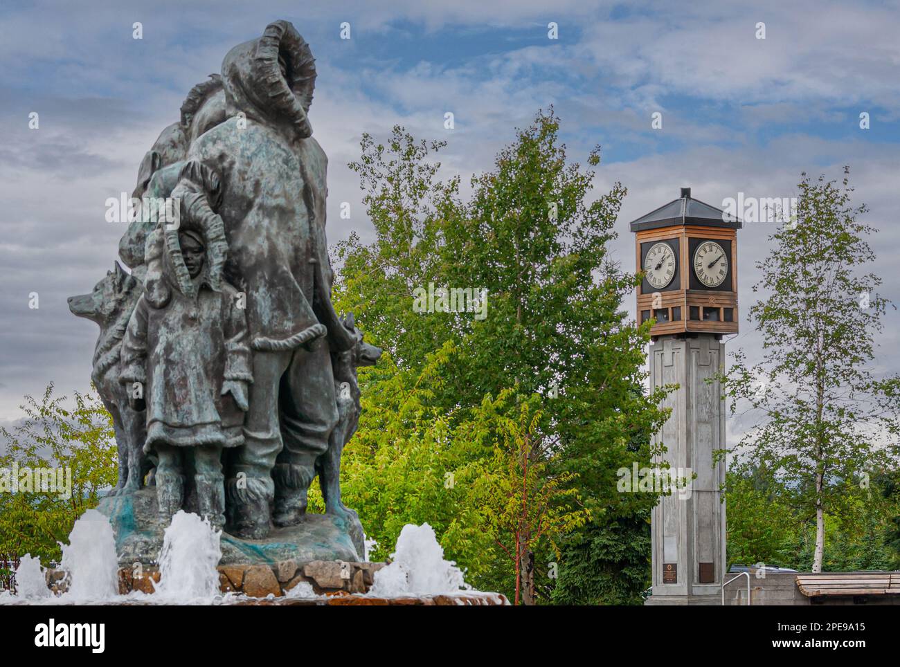Fairbanks, Alaska, USA - 27 luglio 2011: Statua e fontana della prima famiglia sconosciute sul Golden Heart Plaza. Lato bambino e padre, con Torre dell'Orologio rotante Foto Stock