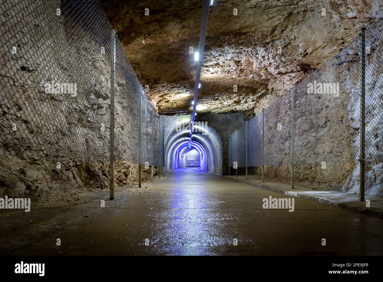 Tunnel di pietra perforato sottoterra nella roccia con illuminazioni blu e recinzione protettiva, uscita dal Prometheus Cave Natural Monument in Georgia. Foto Stock