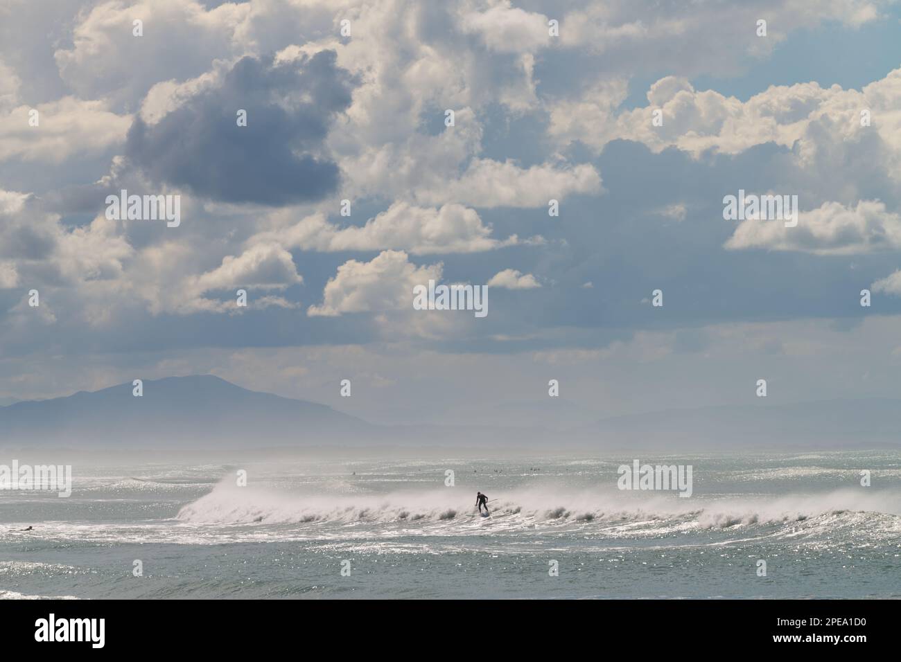 Uomo che naviga un'onda in Nuova Zelanda utilizzando una tavola da pagaiare, Pegasus Bay, con Kaikoura in lontananza, Christchurch Nuova Zelanda. Foto Stock