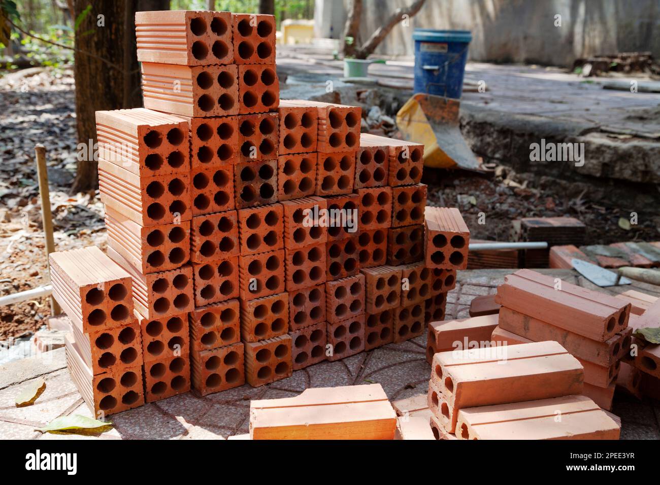 Pila di mattoni cavi arancioni con attrezzi di posa di mattoni in un cantiere. Palo di mattoni di creta bruciati nuovi preparato per lavoro di muratura Foto Stock
