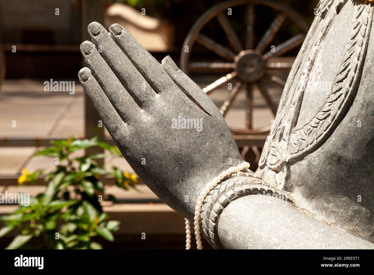 La statua in pietra scolpita offre un primo piano in un tempio buddista con la ruota della vita sullo sfondo. Particolare scultura religiosa, una persona che fa una mudra Foto Stock