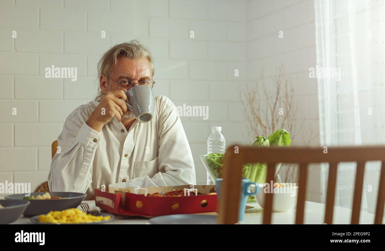Anziano nonno in pensione rimanere a casa con il viso infelice seduta da solo sul tavolo da pranzo in casa. Depresso anziano maturo anziano rovesciato sentirsi solo Foto Stock