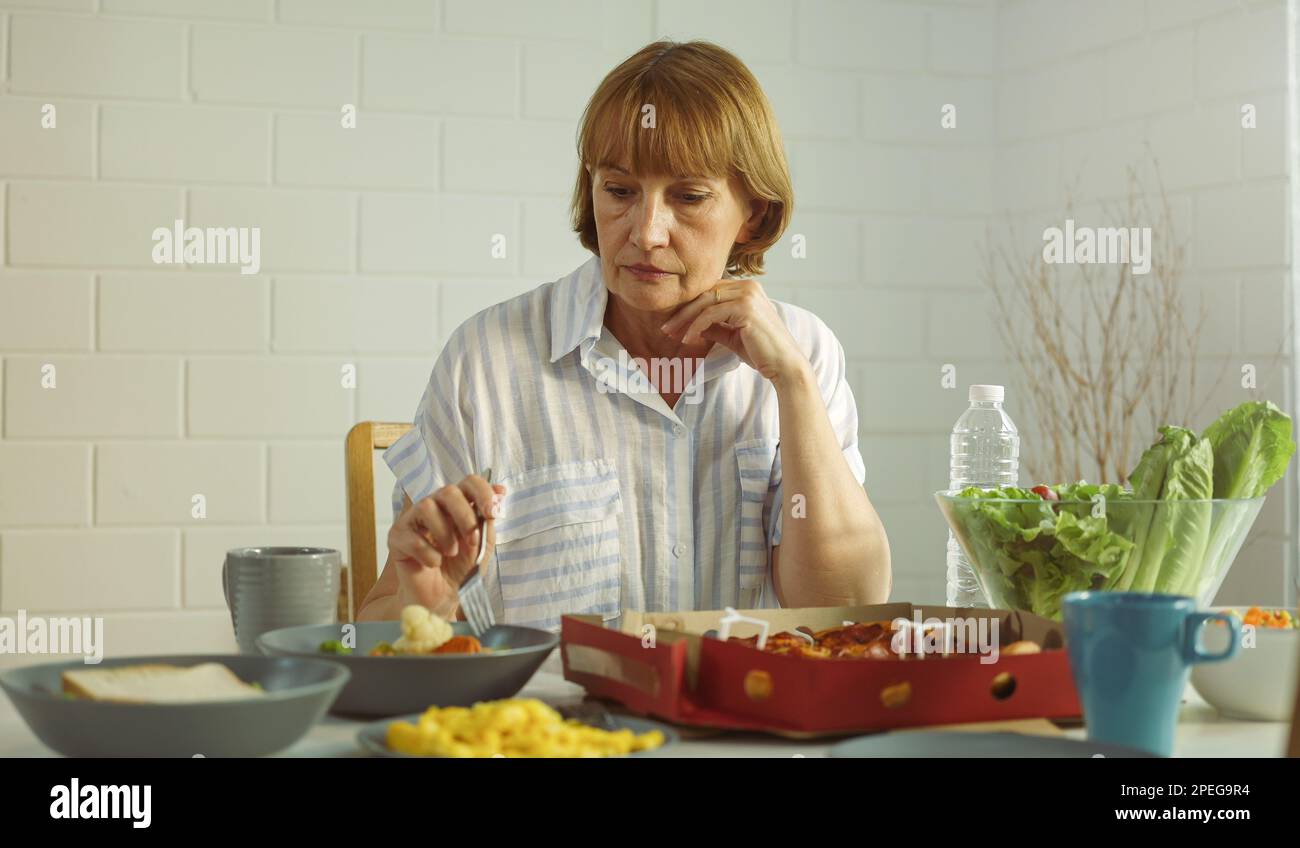 Nonna anziana in pensione rimanere a casa con il viso infelice seduto da solo sul tavolo da pranzo in casa. Depressa matura anziana donna rovesciato sensazione di lon Foto Stock