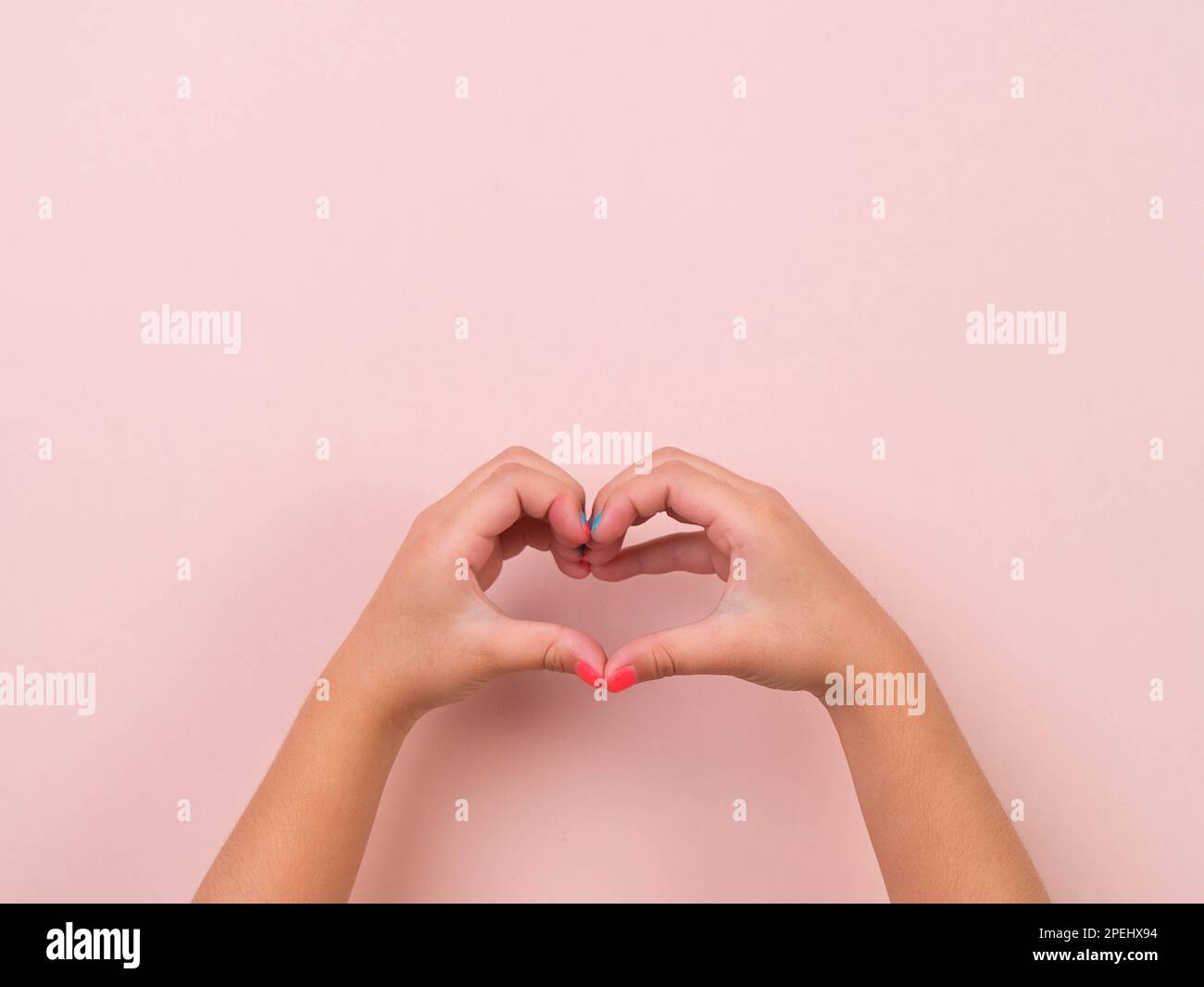 Mano di ragazza che mostra la forma del cuore, l'amore e il simbolo di simpatia su sfondo rosa in studio. Pacchetto di movimenti di gesti e linguaggio del corpo. Foto Stock